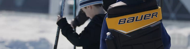Boy standing outside wearing a BAUER GLOVE BACKPACK - 17L, winter apparel and holding a hockey stick