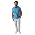 Man wearing a blue patterned polo shirt and white pants on a white background